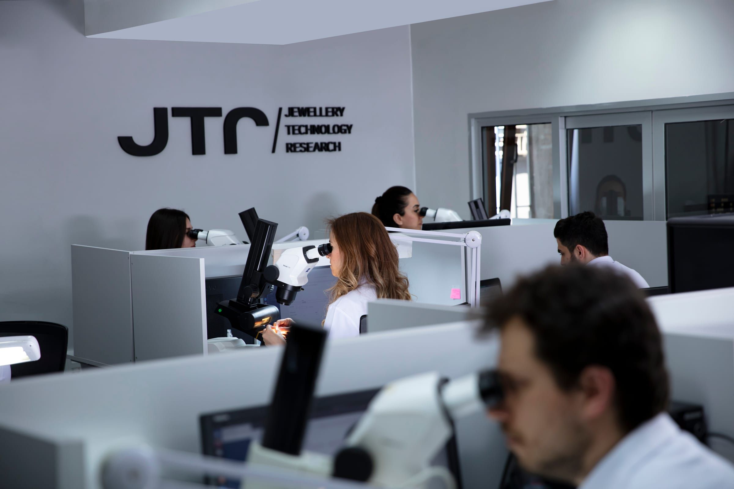 Graders at microscopes in the JTR grading laboratory beneath the JTR wordmark